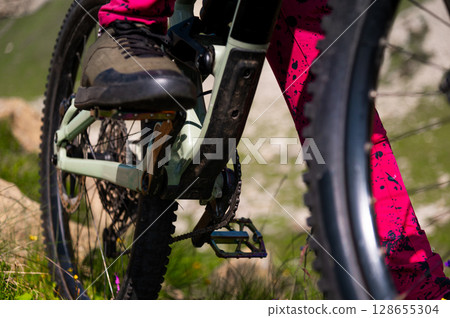 Close-up view of the legs of an unrecognizable rider and the pedals of a bicycle from below. A man in brightly colored clothing stands on a bicycle in the mountains Close-up view of the legs of an unrecognizable rider and the pedals of a bicycle from below. A man in brightly colored clothing stands on a bicycle in the mountains 128655304