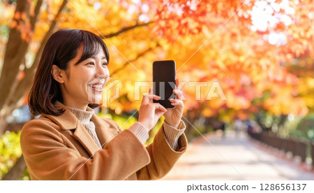 AI 影像：一位年輕女子用智慧型手機拍攝秋葉 128656137