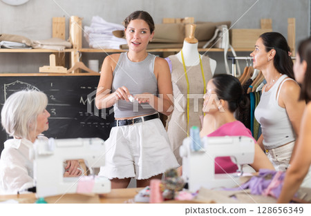 Young female teacher speaking students during dressmaking class Young female teacher speaking students during dressmaking class 128656349
