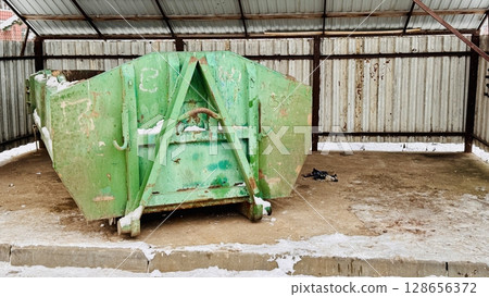 An old green metal container filled with garbage and waste products from residents of an apartment building in the courtyard. Waste management in an urban environment 128656372