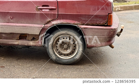An old car that is showing significant rust and wear, complete with a visibly damaged side panel, indicating neglect An old car that is showing significant rust and wear, complete with a visibly damaged side panel, indicating neglect 128656395
