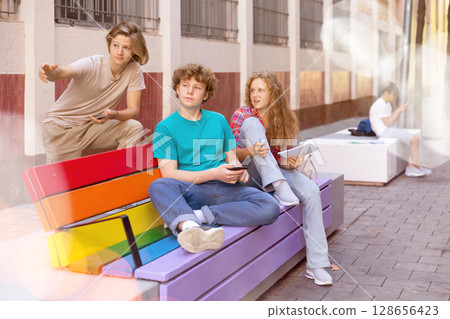 Schoolchildren sitting on bench in schoolyard Schoolchildren sitting on bench in schoolyard 128656423