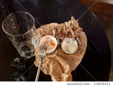 A rather unappealing sight of leftover food scattered haphazardly alongside an empty glass on a table A rather unappealing sight of leftover food scattered haphazardly alongside an empty glass on a table 128656433