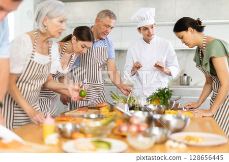 Young guy cook teaches to cook group of people Young guy cook teaches to cook group of people 128656445