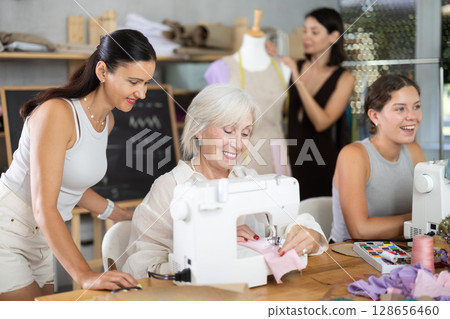 Mature woman stitching fabric on machine in sewing class for adults 128656460