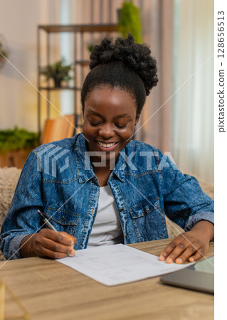 African American woman proudly signs first job contract sitting or invoice smiling with satisfaction African American woman proudly signs first job contract sitting or invoice smiling with satisfaction 128656513