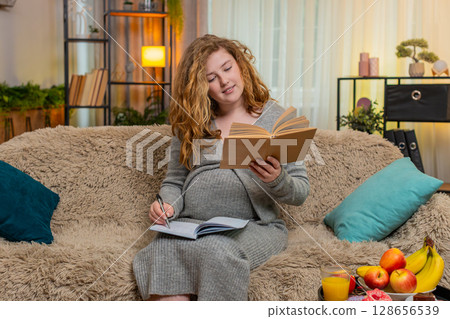 Pregnant woman taking notes from parenting book, focused and concentrated, thoughtful expression Pregnant woman taking notes from parenting book, focused and concentrated, thoughtful expression 128656539