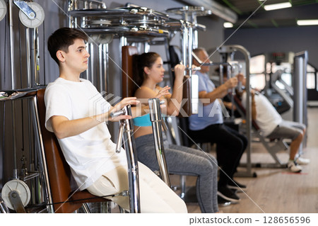 Guy doing chest presses in exercise machine in gym 128656596