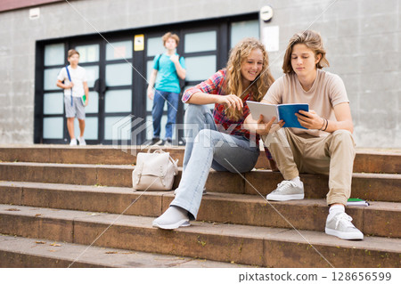 Girl prompts solution to problem to young man sitting on stone staircase in front of school Girl prompts solution to problem to young man sitting on stone staircase in front of school 128656599