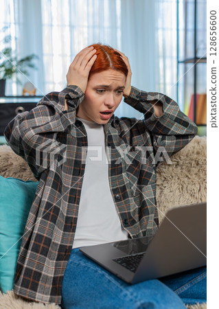 Woman sitting on sofa looking at laptop sadly laying head on arms after bad news or negative result Woman sitting on sofa looking at laptop sadly laying head on arms after bad news or negative result 128656600