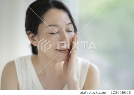 A fifty-year-old woman with her hands on her cheeks and eyes closed Beauty image Portrait 128656608