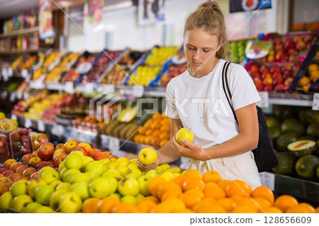 Fifteen-year-old girl chooses apples on the counter Fifteen-year-old girl chooses apples on the counter 128656609