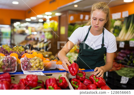 Fifteen-year-old girl who works part-time as a trainee saleswoman puts bell pepper 128656665