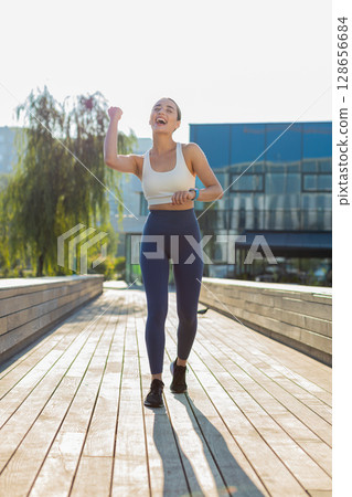 Athletic runner woman looks at smartwatch device fitness bracelet checking heart rate in city park Athletic runner woman looks at smartwatch device fitness bracelet checking heart rate in city park 128656684