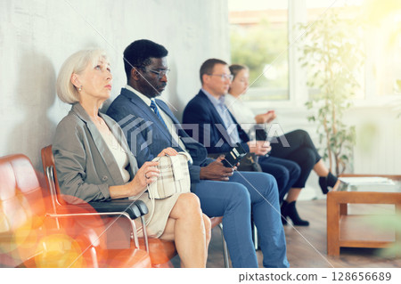 Elderly woman in business suit sits in line at reception Elderly woman in business suit sits in line at reception 128656689