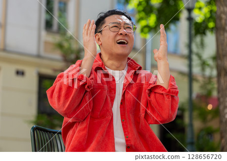 Sad unhappy frustrated Asian man sitting alone in city street, feeling bad, annoyed, grief, problem 128656720