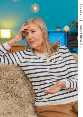 Mature woman placing hand on forehead on sofa showing frustration helplessness after bad day at home Mature woman placing hand on forehead on sofa showing frustration helplessness after bad day at home 128656721