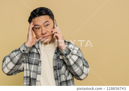 Disinterested tired Asian man having annoyed boring talk on smartphone online conversation quarrel Disinterested tired Asian man having annoyed boring talk on smartphone online conversation quarrel 128656743