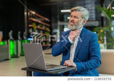 Sick businessman talking on video call having sore throat, coughs sitting with laptop in lobby Sick businessman talking on video call having sore throat, coughs sitting with laptop in lobby 128656758