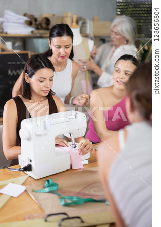 Young woman sewing with stitching-machine controlled by teacher 128656804
