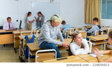 Teenage boys and girls friendly talking in break between lessons Teenage boys and girls friendly talking in break between lessons 128656813