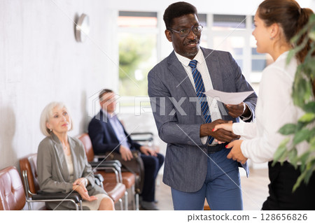 Woman makes deal, shaking hands with middle-aged African man colleague while standing in office Woman makes deal, shaking hands with middle-aged African man colleague while standing in office 128656826