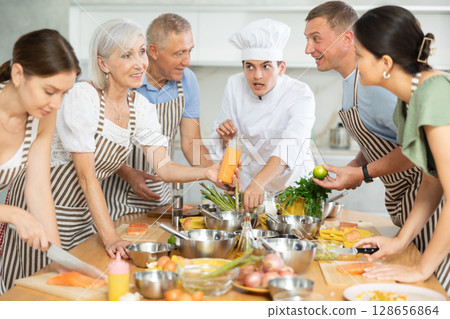 Young guy cook teaches to cook group of people Young guy cook teaches to cook group of people 128656864