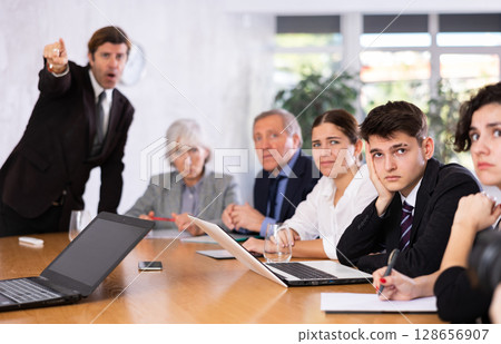 Frustrated guy sitting in office with coworkers and irritated boss Frustrated guy sitting in office with coworkers and irritated boss 128656907