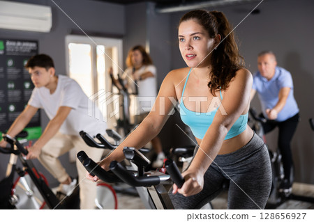 Young girl doing cardio training on stationary bike in gym Young girl doing cardio training on stationary bike in gym 128656927