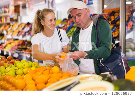 Man with a fifteen-year-old girl choose oranges at the counter Man with a fifteen-year-old girl choose oranges at the counter 128656953