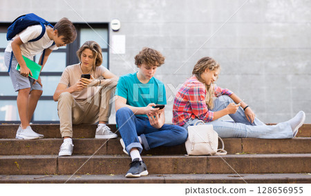Teenager girl and boys sitting front college with smartphones 128656955