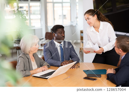 Young woman head of department speaks at meeting ahead frowning colleagues 128657004