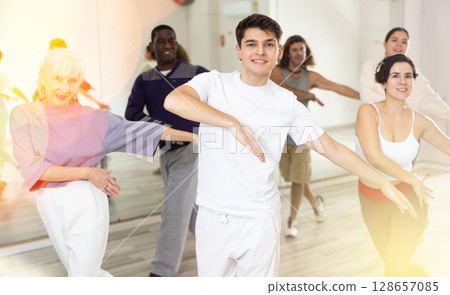 Cheerful guy practicing modern vigorous dance with group Cheerful guy practicing modern vigorous dance with group 128657085