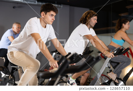 Young guy doing cardio workout on exercise bike in gym Young guy doing cardio workout on exercise bike in gym 128657110
