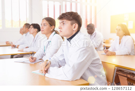 Young medical student taking notes during group lecture in university 128657112