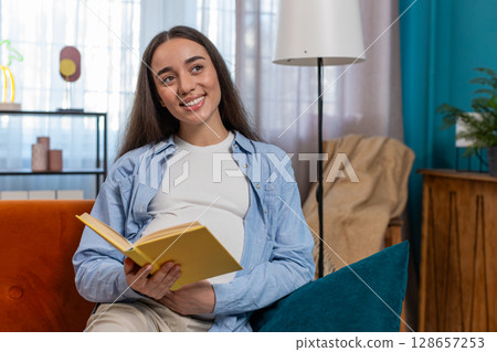 Pregnant Caucasian woman reading book advice child care guide feeling relax on cozy couch at home Pregnant Caucasian woman reading book advice child care guide feeling relax on cozy couch at home 128657253
