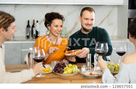 Two married couples are sitting at table, enjoying food and wine, chatting, talking, laughing. 128657501