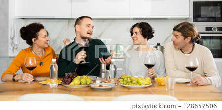 Two married couples are sitting at table, enjoying food and wine, chatting, talking, laughing. 128657506