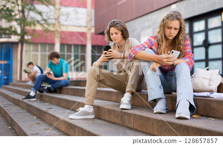 Boy and girl teens sitting on stairs and using smartphones 128657857