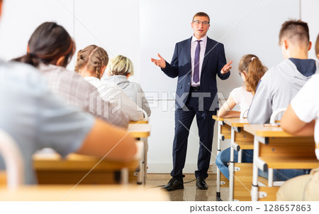 Man teacher with notebook is giving interesting lecture for students in classroom Man teacher with notebook is giving interesting lecture for students in classroom 128657863