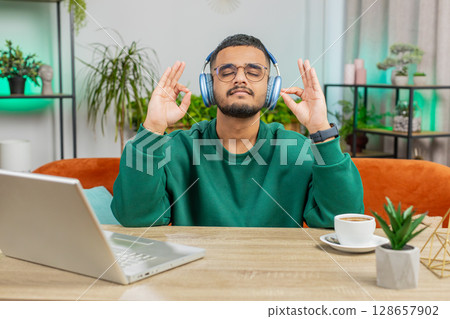 Indian man listening music, breathes deeply meditating with concentrated thoughts peaceful at home 128657902