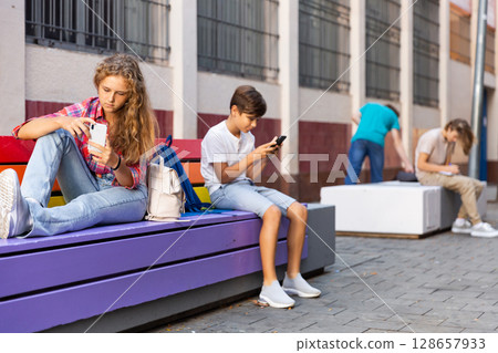 Boy and girl using gadgets during break at school Boy and girl using gadgets during break at school 128657933
