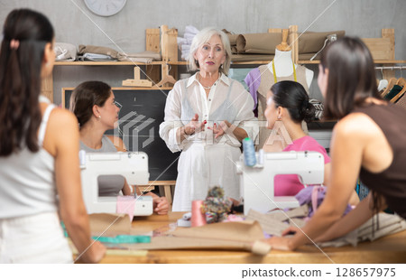 Female teacher explaining pattern structure by chalkboard during sewing course for adults 128657975
