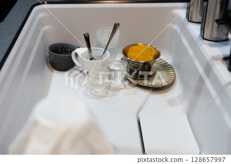 A stylish system kitchen with indirect lighting and a black base, a dishwasher and sink, and an induction cooking heater A stylish system kitchen with indirect lighting and a black base, a dishwasher and sink, and an induction cooking heater 128657997