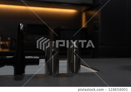 A stylish system kitchen with indirect lighting and a black base, a dishwasher and sink, and an induction cooking heater A stylish system kitchen with indirect lighting and a black base, a dishwasher and sink, and an induction cooking heater 128658001