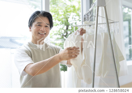 Smiling man in his 50s hanging out laundry, looking at camera Smiling man in his 50s hanging out laundry, looking at camera 128658024