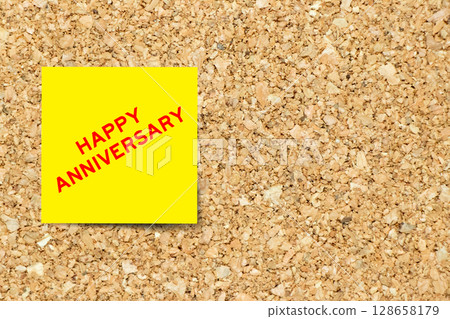 Yellow note paper with word happy anniversary on cork board background with copy space 128658179