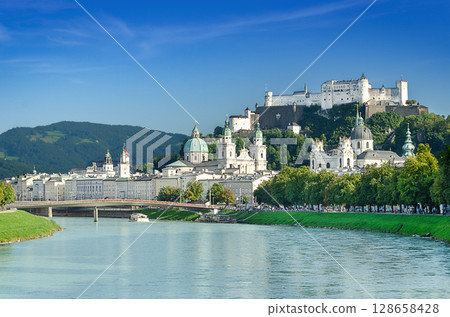 Salzburg, festival city in Austria. Iconic view of the old town on Salzach River, with Baroque Salzburg Cathedral in the middle, Collegiate Church to the right, and Hohensalzburg Fortress in the back. 128658428