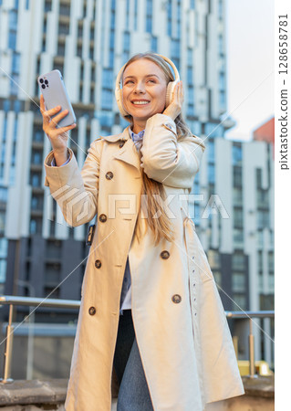 Happy mature businesswoman in headphones listening favorite energetic music on smartphone on street Happy mature businesswoman in headphones listening favorite energetic music on smartphone on street 128658781