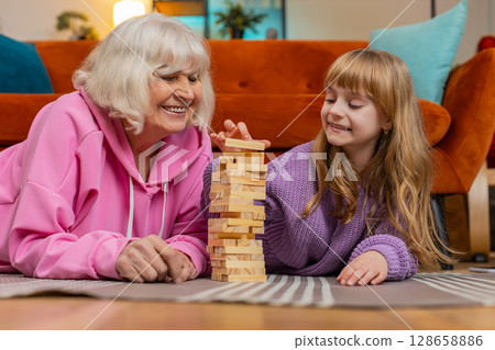 Excited little cute girl granddaughter playing building block game with smiling senior grandmother Excited little cute girl granddaughter playing building block game with smiling senior grandmother 128658886